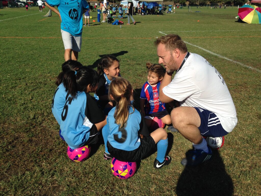 A group of young girls sitting on the ground with an adult.